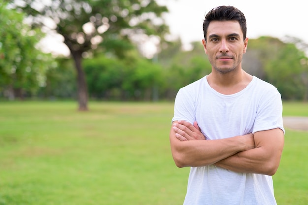 Young handsome Hispanic man with arms crossed in the park outdoor