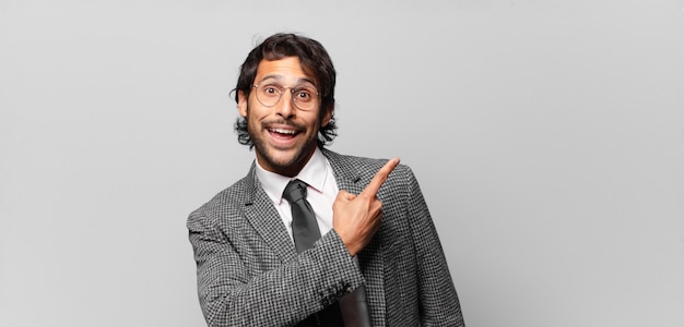 Young handsome indian man looking excited and surprised pointing to the side and upwards to copy space. business concept