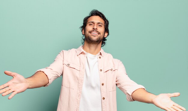 Photo young handsome indian man smiling cheerfully giving a warm, friendly, loving welcome hug, feeling happy and adorable