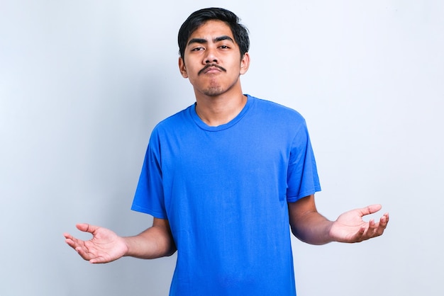 Young handsome Indian man wearing casual shirt over white background clueless and confused expression with arms and hands raised. Doubt concept.