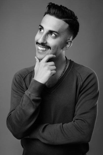  young handsome Iranian man with mustache with long sleeved shirt against gray wall in black and white