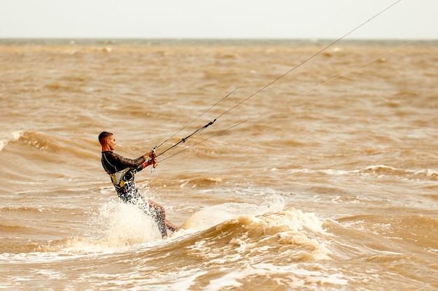 Young handsome kiteboarder rides the waves