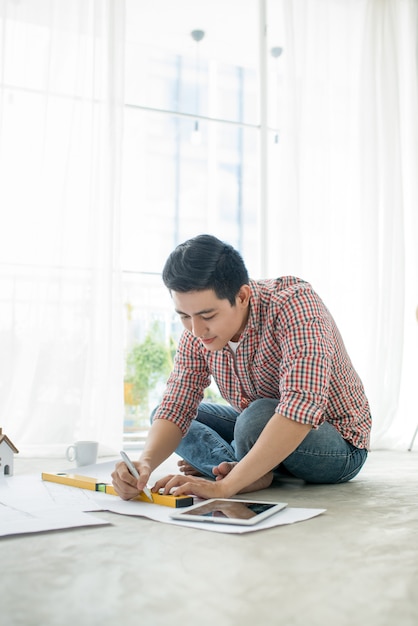 Young handsome male asian architect working at home on the floor.