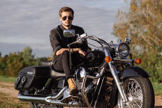 Young handsome male biker is sitting on his motor bike outdoors at the lake background