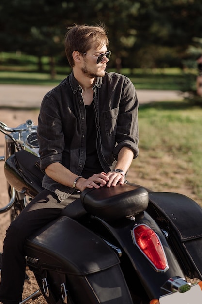 Young handsome male biker is sitting on his motor bike outdoors at the lake background