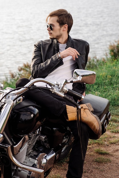 Young handsome male biker is sitting and smoking on motor bike