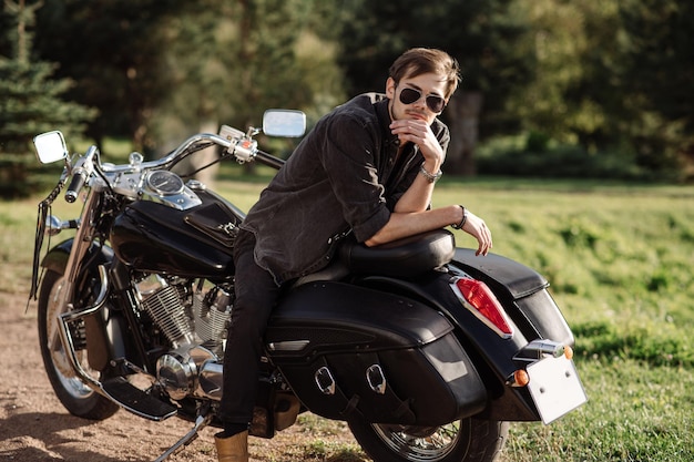 Young handsome male is sitting on his motor bike outdoors