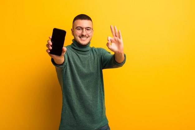 Young handsome man  against flat wall with a smart phone