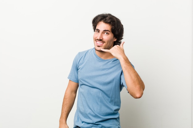 Young handsome man against a white space showing a mobile phone call gesture with fingers.