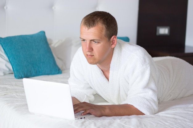 Young handsome man in bathrobe using laptop in hotel room