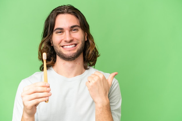 Young handsome man brushing teeth over isolated background pointing to the side to present a product