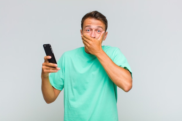 Young handsome man covering mouth with hands with a shocked, surprised expression