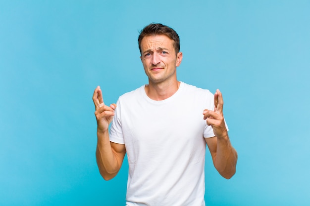 Young handsome man crossing fingers anxiously and hoping for good luck with a worried look