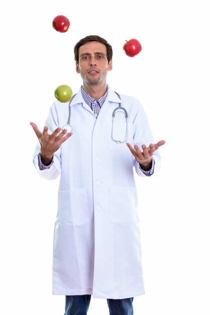 young handsome man doctor standing while juggling green apple and two red apples