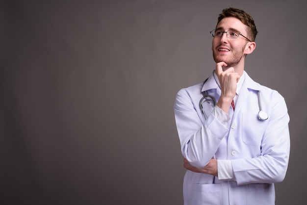 Young handsome man doctor wearing eyeglasses against gray