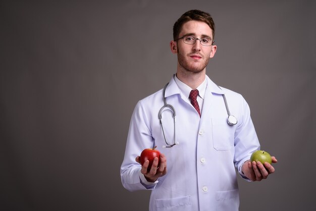 Young handsome man doctor wearing eyeglasses against gray