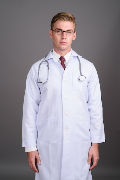 Young handsome man doctor with blond hair on grey wall