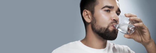 Young handsome man drinking fresh water against gray background