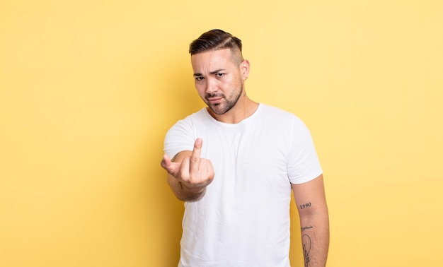 Young handsome man feeling angry, annoyed, rebellious and aggressive, flipping the middle finger, fighting back