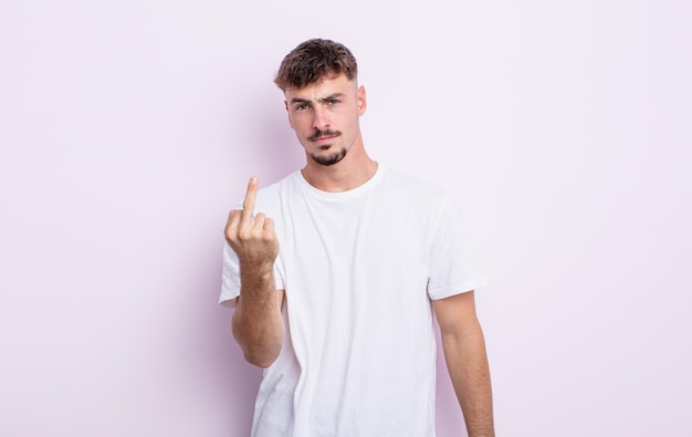 Young handsome man feeling angry, annoyed, rebellious and aggressive, flipping the middle finger, fighting back