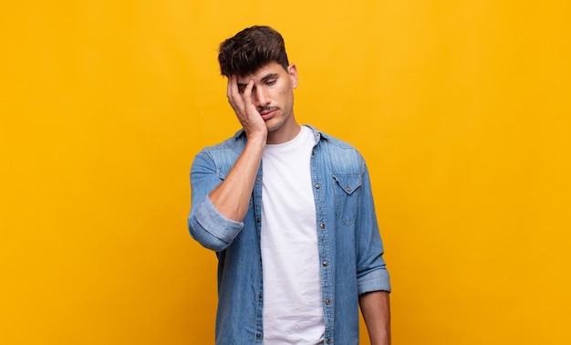 Young handsome man feeling bored, frustrated and sleepy after a tiresome, dull and tedious task, holding face with hand