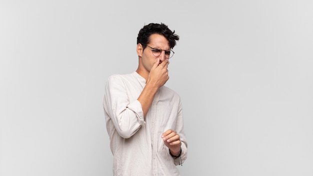 Young handsome man feeling disgusted, holding nose to avoid smelling a foul and unpleasant stench