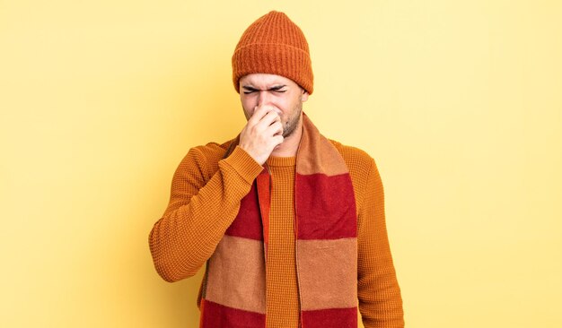 Young handsome man feeling disgusted, holding nose to avoid smelling a foul and unpleasant stench