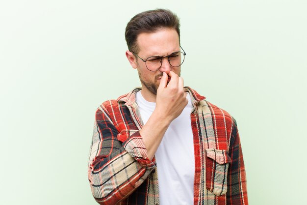 Young handsome man feeling disgusted, holding nose to avoid smelling a foul and unpleasant stench