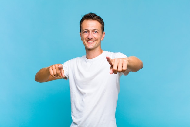 Young handsome man feeling happy and confident, pointing to camera with both hands and laughing