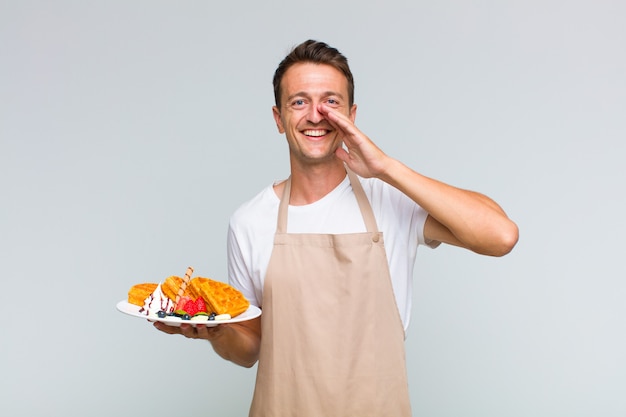 Young handsome man feeling happy, excited and positive, giving a big shout out with hands next to mouth, calling out