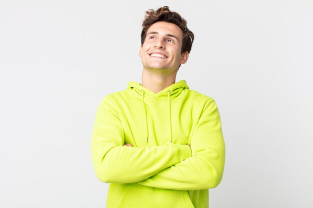 Young handsome man feeling happy, proud and hopeful, wondering or thinking, looking up to copy space with crossed arms