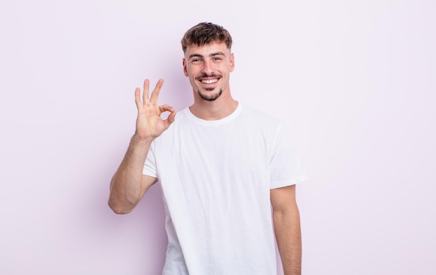 Young handsome man feeling happy, relaxed and satisfied, showing approval with okay gesture, smiling