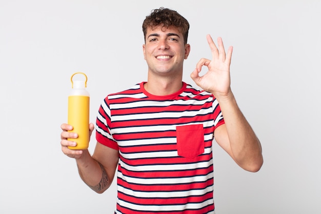 Young handsome man feeling happy, showing approval with okay gesture and holding a coffee thermos