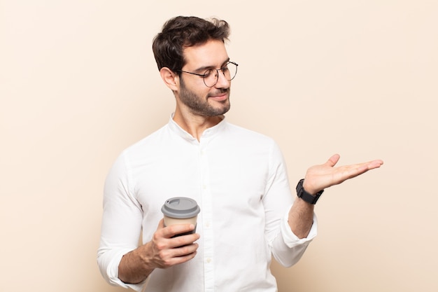 Young handsome man feeling happy and smiling casually, looking to an object or concept held on the hand on the side