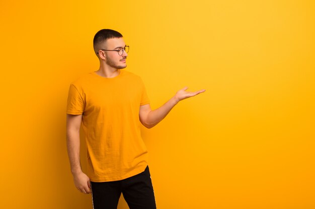 Young handsome man feeling happy and smiling casually, looking to an object or concept held on the hand on the side