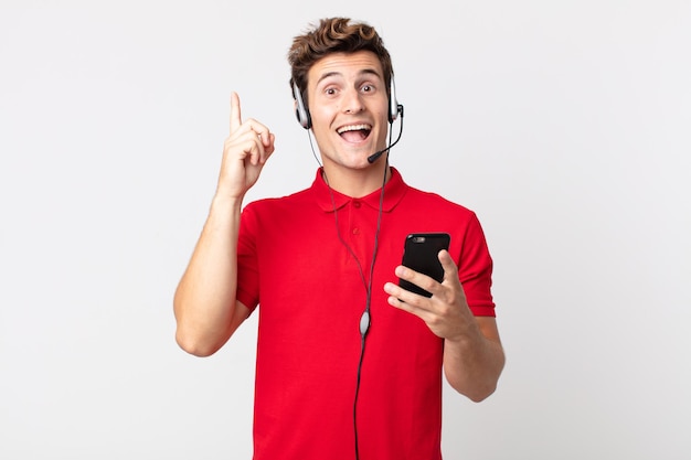 Young handsome man feeling like a happy and excited genius after realizing an idea with a smartphone and headset