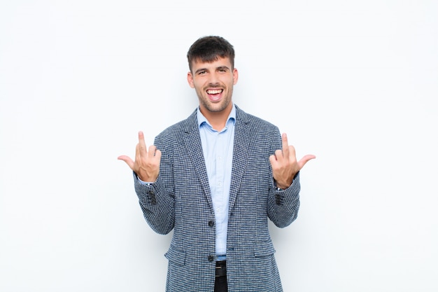 Young handsome man feeling provocative, aggressive and obscene, flipping the middle finger, with a rebellious attitude against white wall