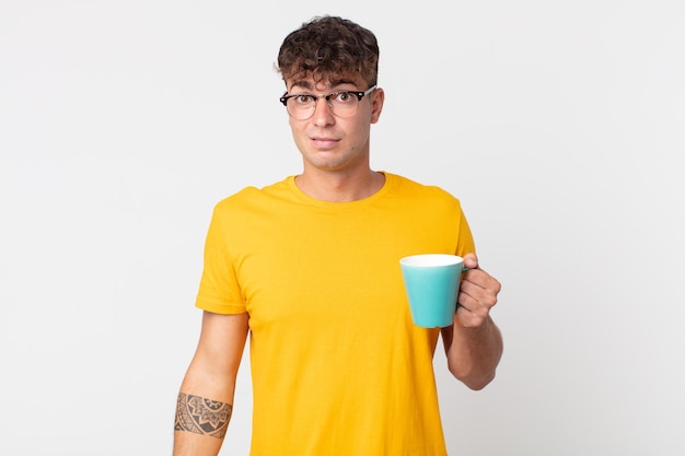 young handsome man feeling puzzled and confused and holding a coffe cup