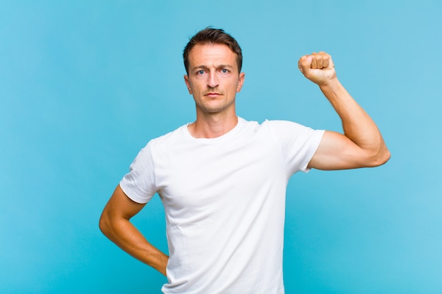 Young handsome man feeling serious, strong and rebellious, raising fist up, protesting or fighting for revolution