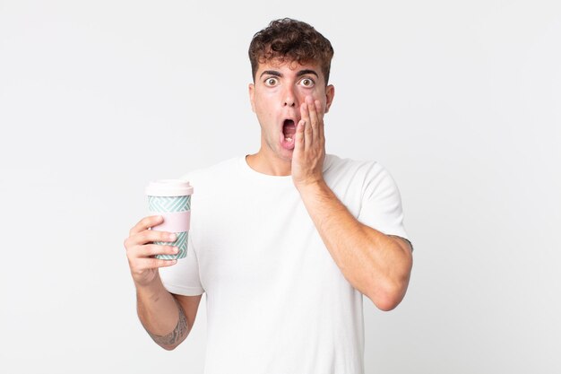 young handsome man feeling shocked and scared and holding a take away coffee