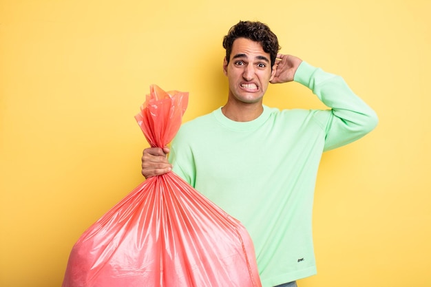 Young handsome man feeling stressed, anxious or scared, with hands on head. trash bag concept