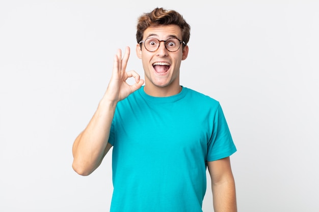 Young handsome man feeling successful and satisfied, smiling with mouth wide open, making okay sign with hand