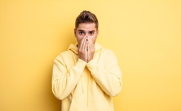 Young handsome man feeling worried, upset and scared, covering mouth with hands, looking anxious and having messed up. strange moustache concept