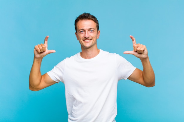 Young handsome man framing or outlining own smile with both hands, looking positive and happy, wellness concept