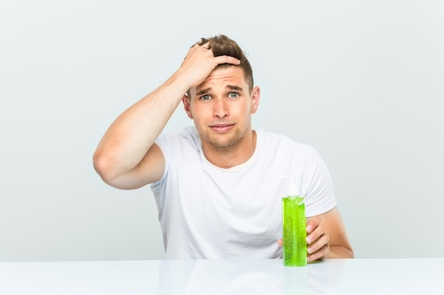 Young handsome man holding a aloe vera bottle being shocked, she has remembered important meeting.