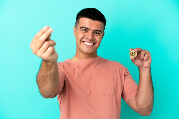 Young handsome man holding a Bitcoin over isolated blue background making money gesture