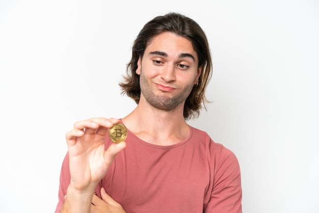 Young handsome man holding a Bitcoin isolated on white background with sad expression