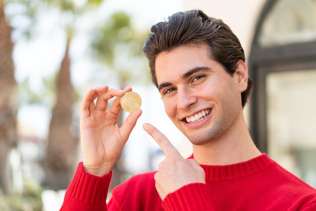 Young handsome man holding a Bitcoin and pointing it