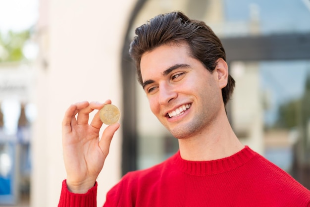 Young handsome man holding a Bitcoin with happy expression