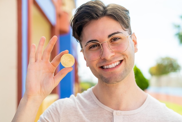 Young handsome man holding a Bitcoin with happy expression